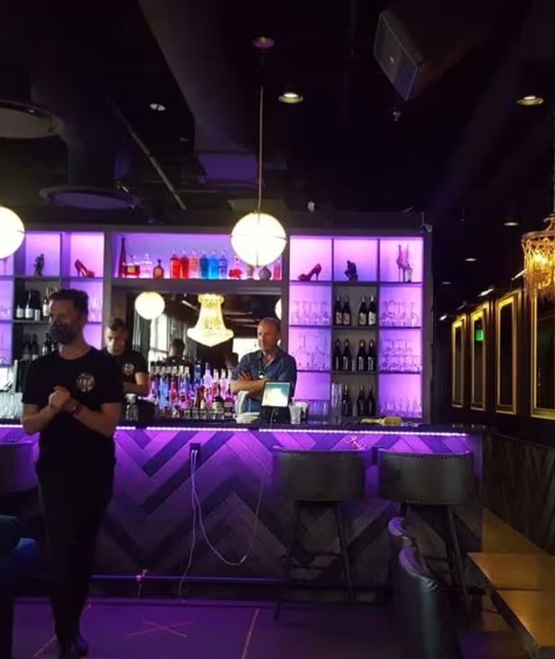A man standing in front of a bar with a laptop computer on its counter and a woman standing in front of the bar.
