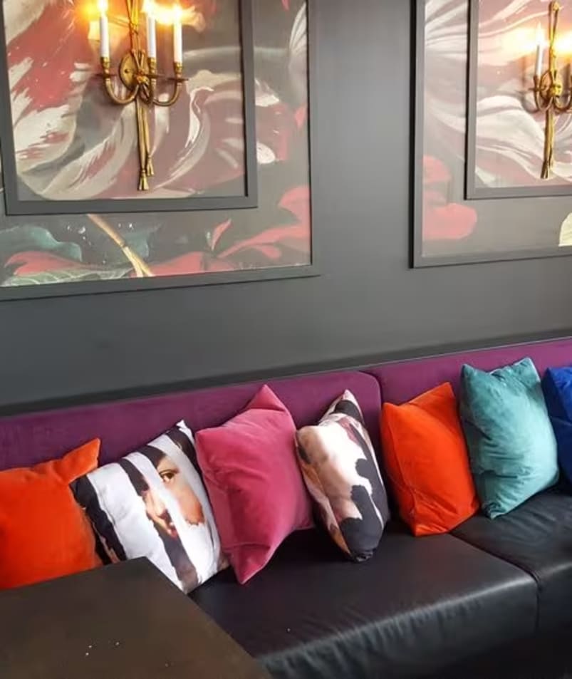 A couch with a bunch of pillows on it next to a table with chairs and a lamp on it at the Friends of Dorothy Lounge in Kelowna.