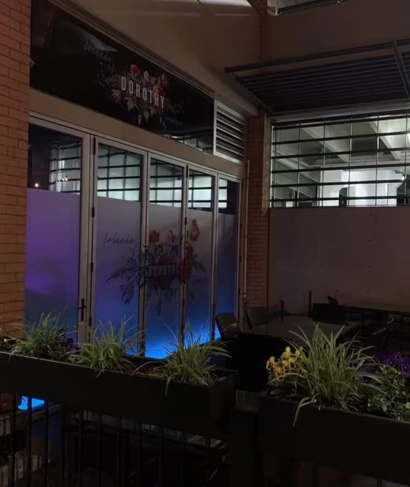 A brick building with plants growing out of its sides and a neon sign above the door that says, Friends of Dorothy Lounge in Kelowna.