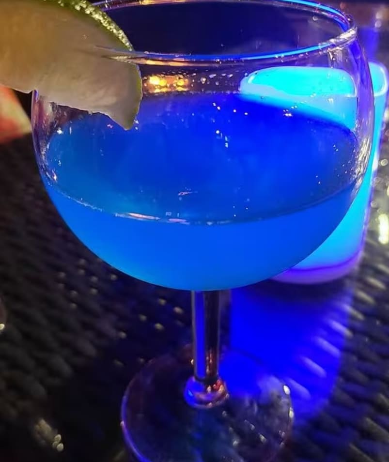a close up of a blue drink in a glass on a table with a lime slice on the rim