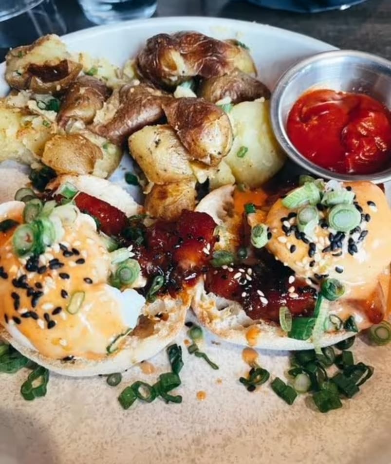 a plate of food that includes eggs, potatoes, tomatoes and other toppings, and a small bowl of ketchup.