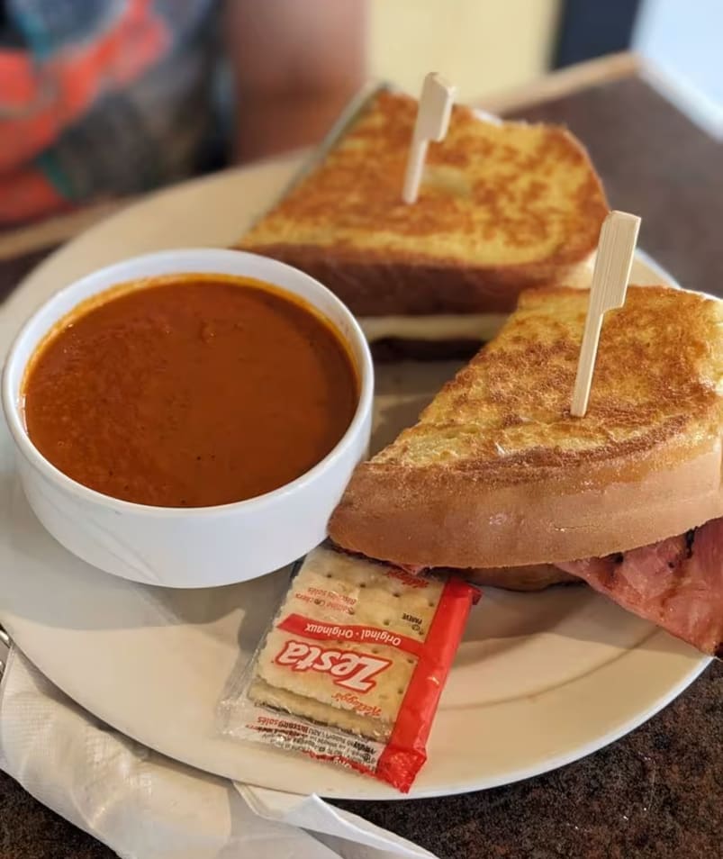 A grilled cheese sandwich paired with a bowl of tomato soup, accompanied by saltine crackers on a white plate at The Jammery in Lake Country.