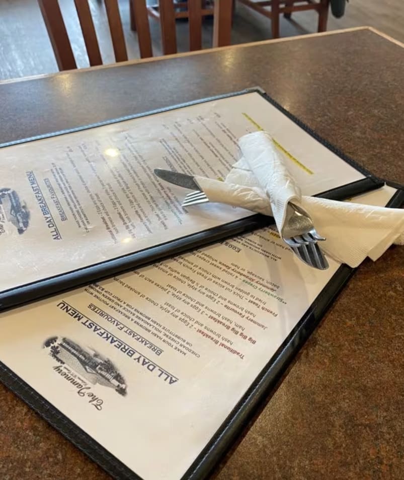 A set of menus from The Jammery in Lake Country, with neatly wrapped cutlery on top, placed on a wooden table.