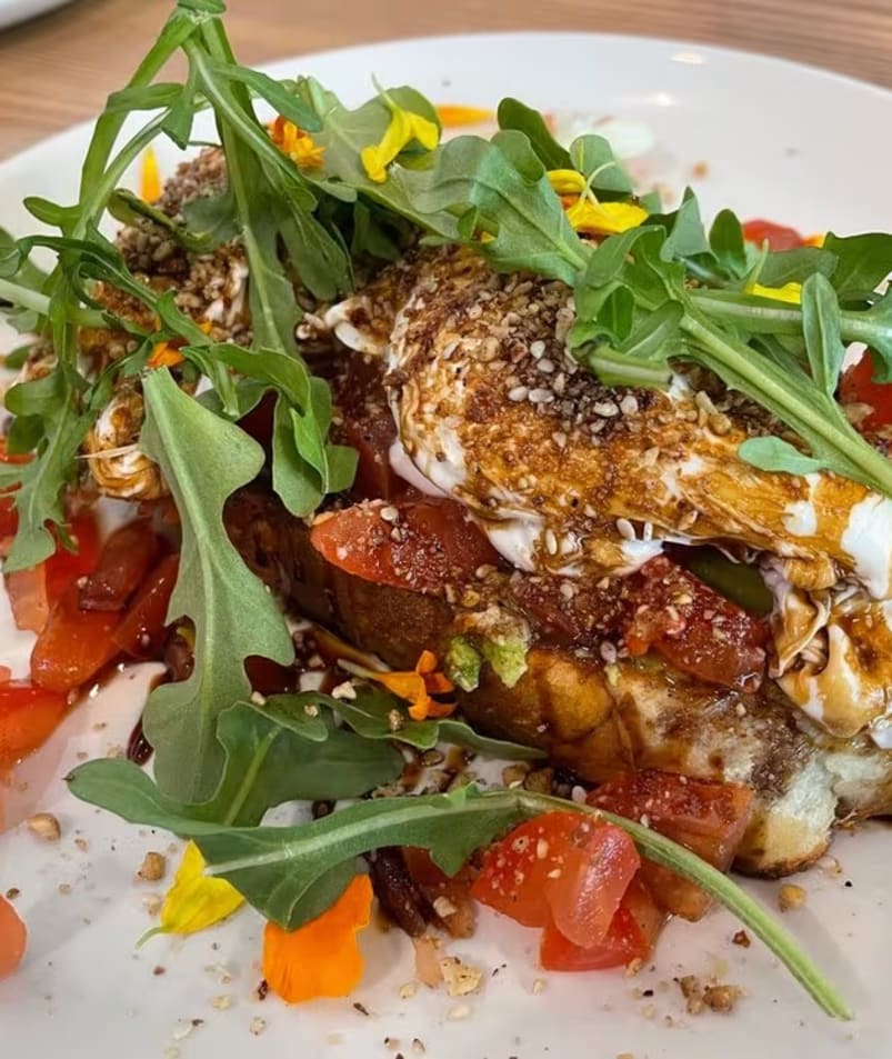 A plate of gourmet toast topped with tomatoes, arugula, seeds, and drizzled sauce, served at The Jammery in Lake Country.