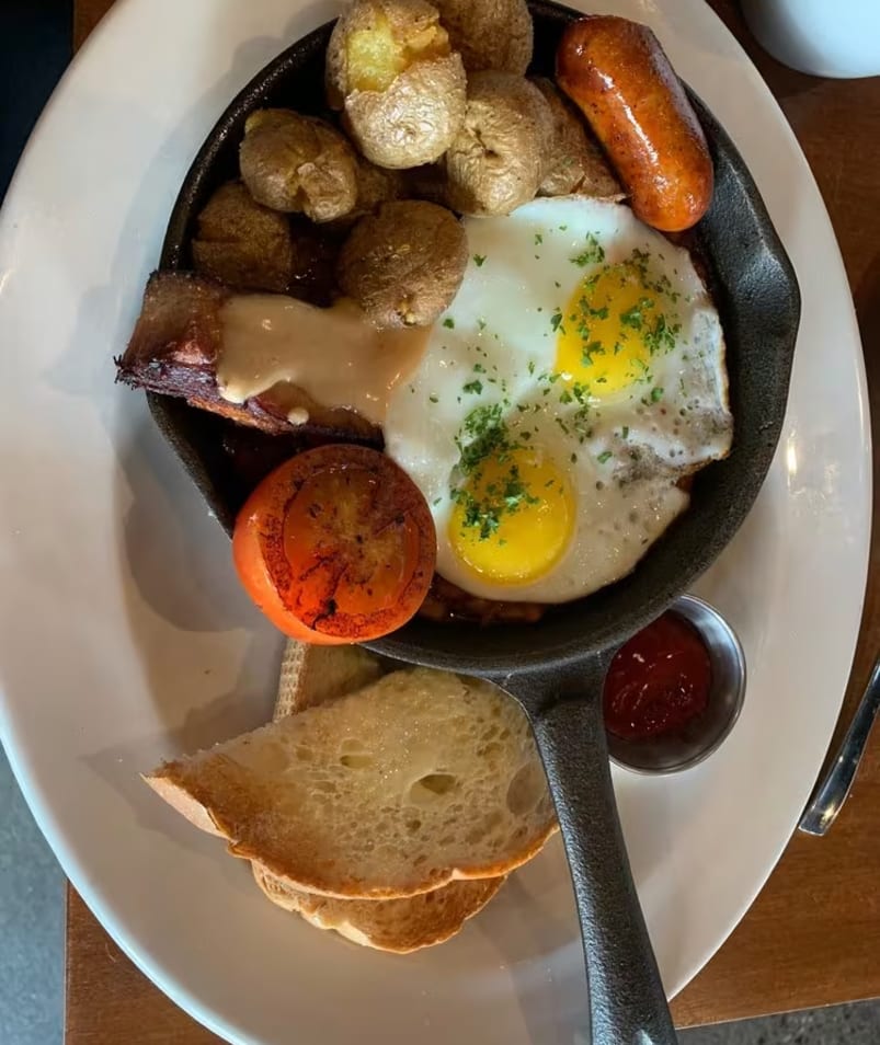 A skillet with breakfast items including eggs, potatoes, sausage, toast, and a grilled tomato from The Jammery in Lake Country.