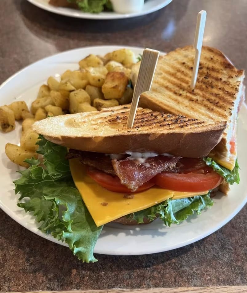 A sandwich with bacon, cheese, tomato, lettuce, and mayonnaise is served with a side of roasted potatoes at The Jammery in Lake Country.