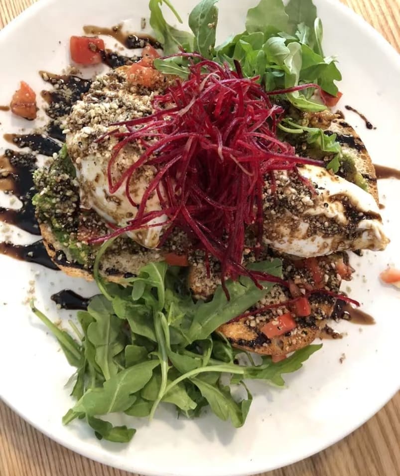 A colorful plate of gourmet toast topped with poached eggs, fresh greens, and beetroot, drizzled with a balsamic glaze, served at The Jammery in Lake Country.