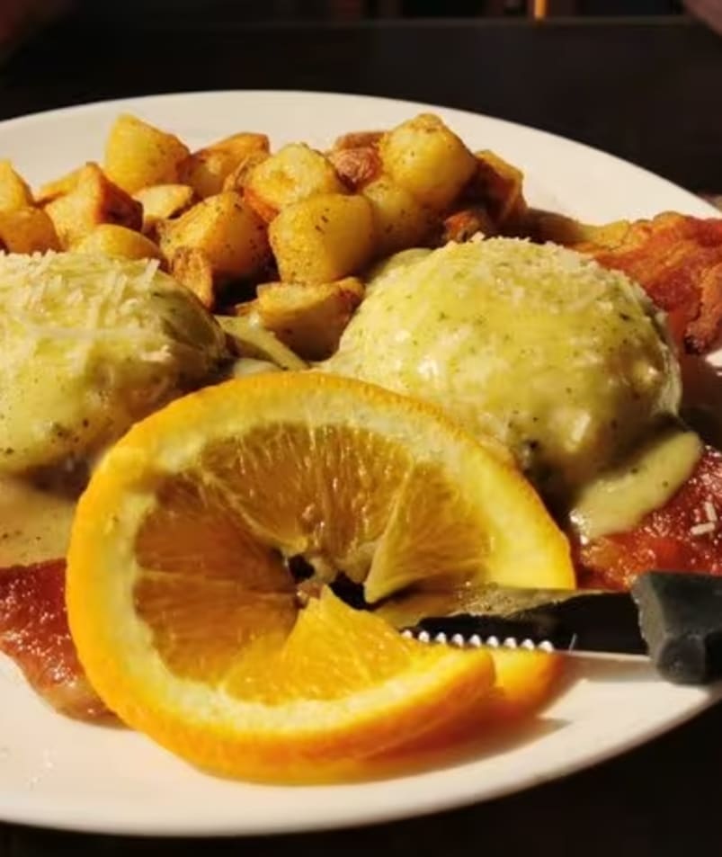 A plate of Eggs Benedict with home fries and an orange garnish served at The Jammery in Lake Country.