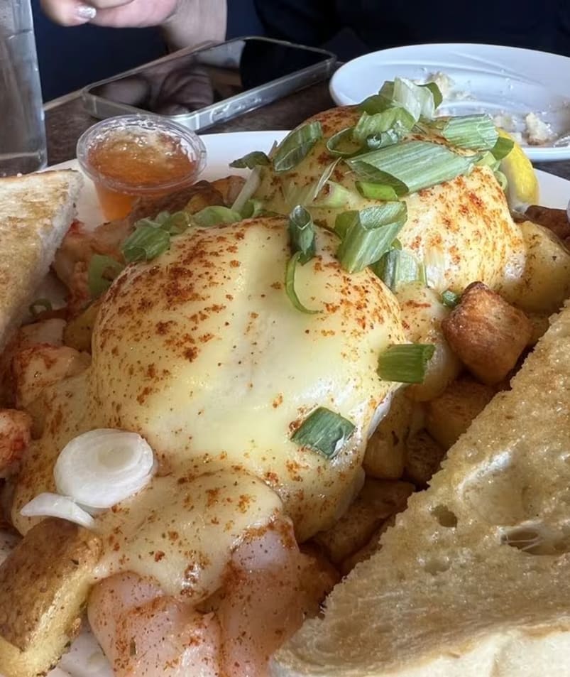A close-up shot of a gourmet breakfast plate from The Jammery in Lake Country, featuring a cheesy omelette topped with green onions, toast on the side, and accompanied by sauces.