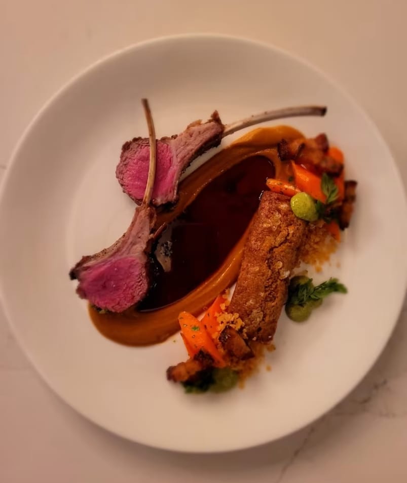 A plated gourmet meal featuring lamb chops, a rich brown sauce, and vegetable garnishes at Erica Jane Restaurant in Kelowna.