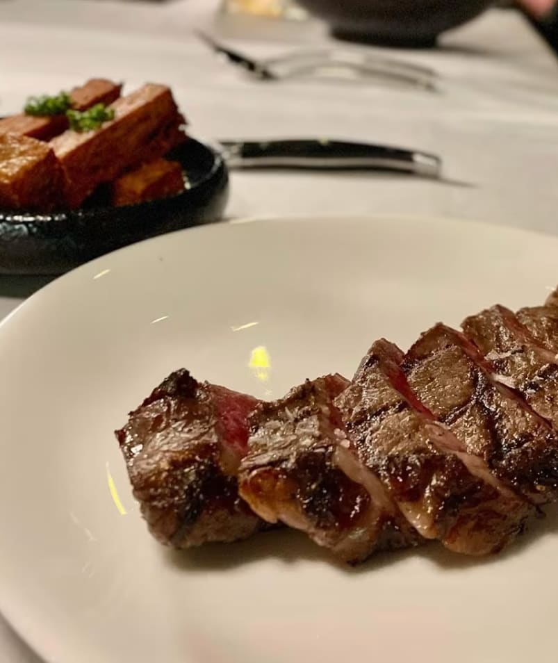 Sliced steak on a white plate with crispy potato wedges in a dark dish, served at Erica Jane Restaurant in Kelowna.