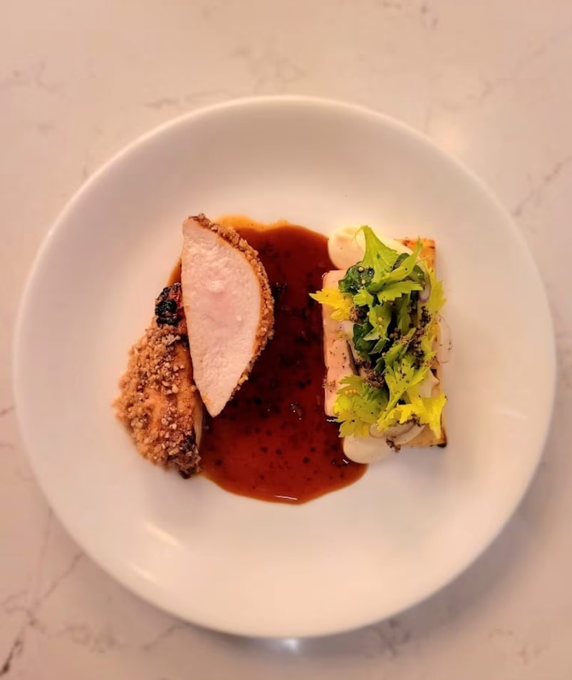 A gourmet dish with a piece of roasted meat, a savory sauce, and a garnish of greens served on a white plate at Erica Jane Restaurant in Kelowna.