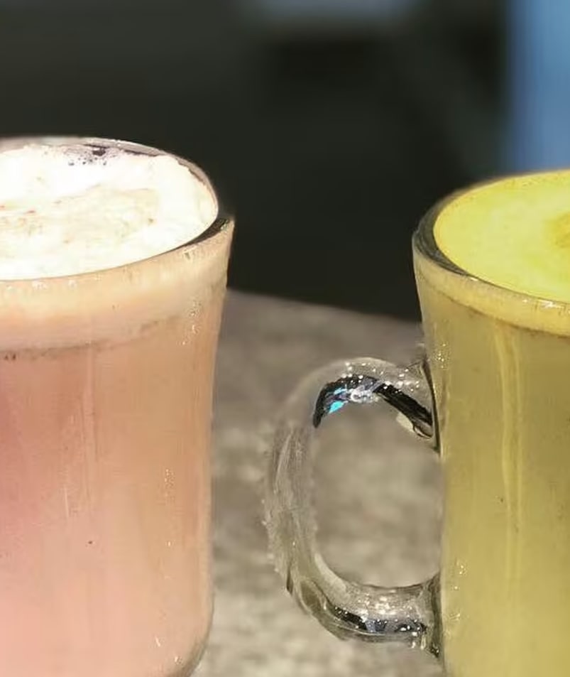 A couple of glasses filled with liquid on top of a marble countertop next to a cup filled with liquid.