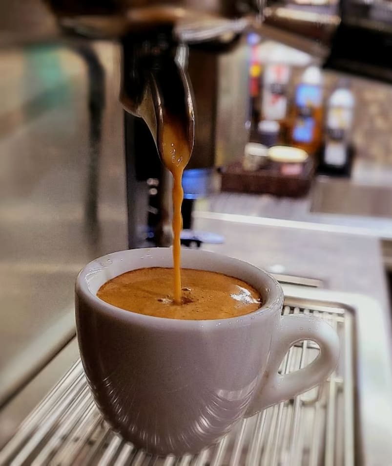 a cup of coffee being poured into a cup of coffee on top of a metal rack in a coffee shop