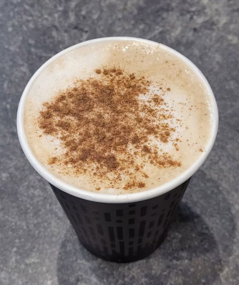 a cup of coffee with cinnamon sprinkles in it sitting on a countertop next to a cup of coffee.