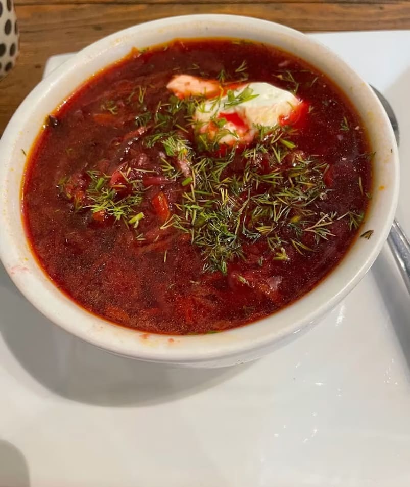 a bowl of soup on a white plate with a spoon and a cup of coffee on the side of the plate.