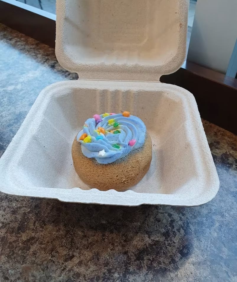 A cupcake with blue frosting in a foam container on a table next to a box of donuts at Half Blind Bean Coffee in Kelowna.