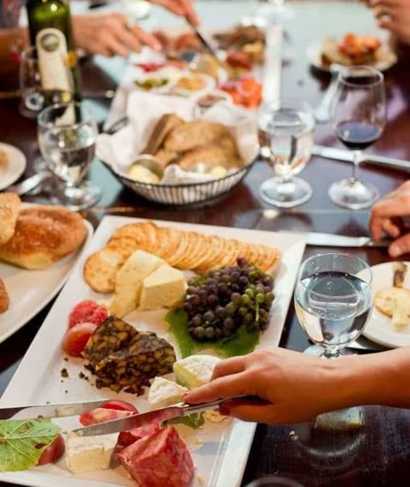 a group of people sitting at a table with plates of food and glasses of wine in front of them