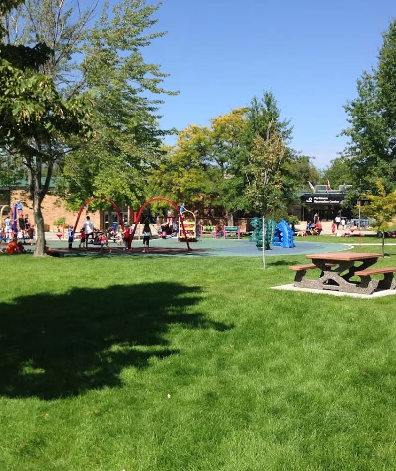 A childrens play area in the middle of a park with a play structure and childrens swings at Parkinson Recreation Centre in Kelowna.