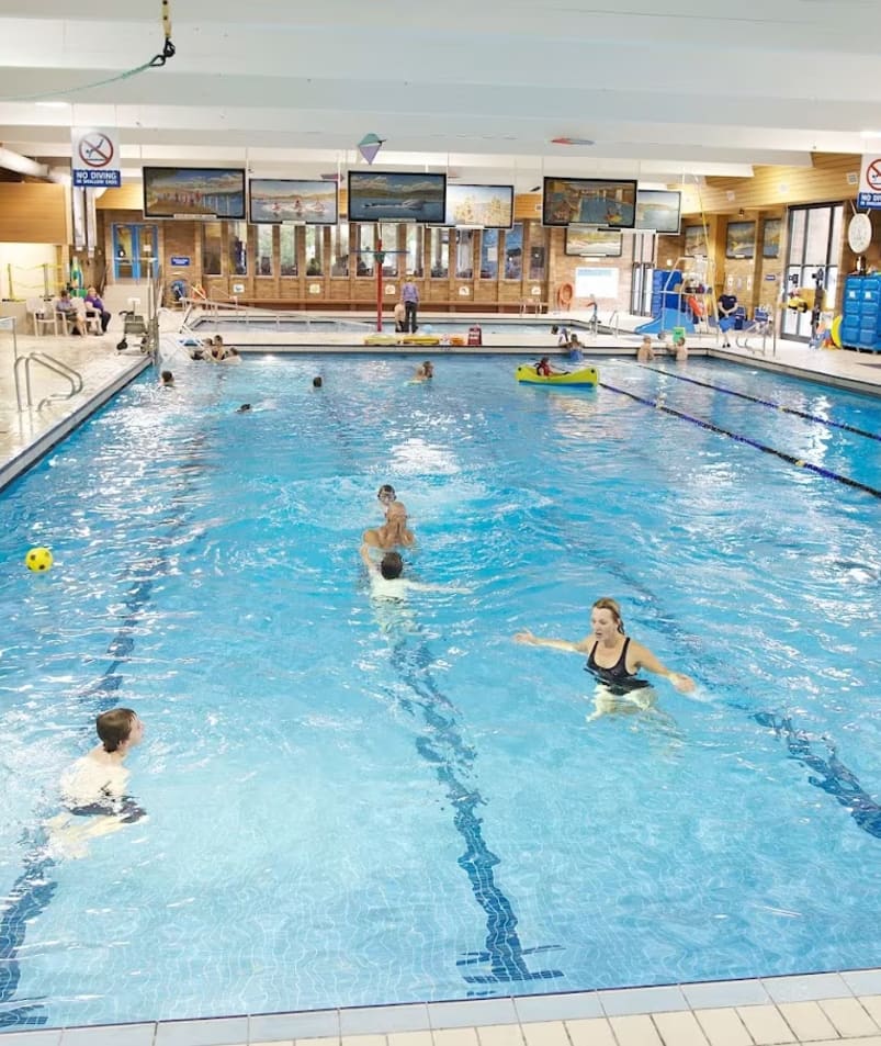 a group of people in a swimming pool playing with a frisbee and water slide in the background