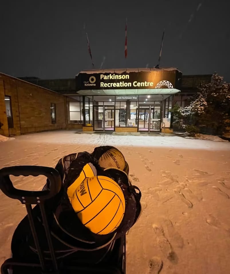 a yellow and black ball sitting on top of a bag in the middle of a snow-covered parking lot in front of the Parkinson Recreation Centre in Kelowna