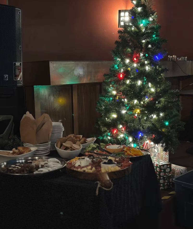 A Christmas tree is lit up in a room with food on a table and a Christmas tree in the background at Rusty's Sports Lounge in Kelowna.