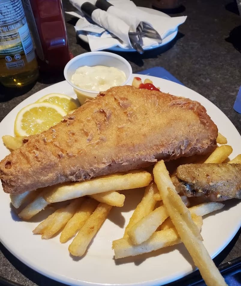 a white plate topped with fish and fries next to a bowl of sauce and a bottle of ketchup