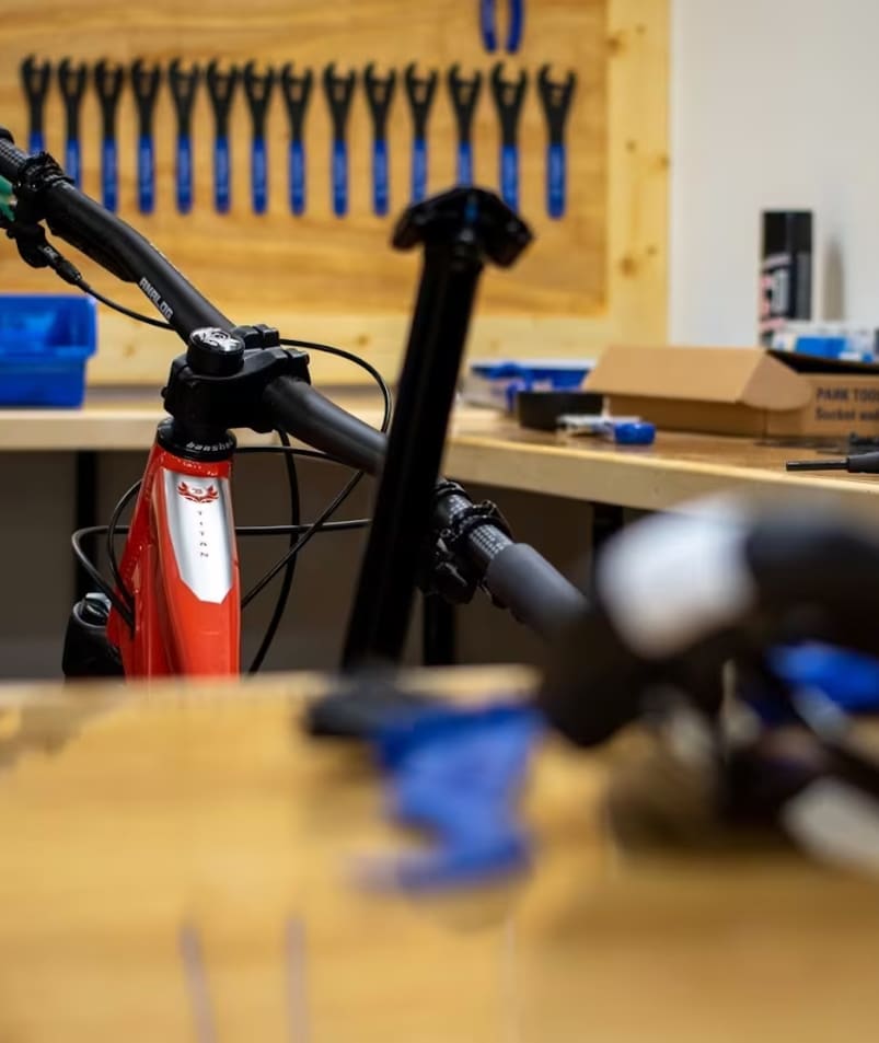 a bicycle parked in a garage next to a workbench with tools on the counter and a wrench on the back of the bike