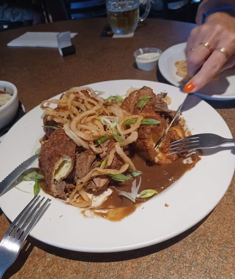 a plate of food with meat and noodles on a table with a person holding a fork and a knife