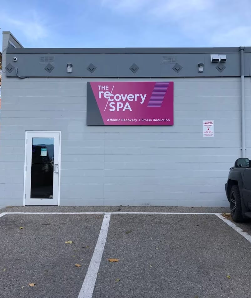 Exterior view of The Recovery Spa in Kelowna with a parked vehicle and autumn leaves on the ground.