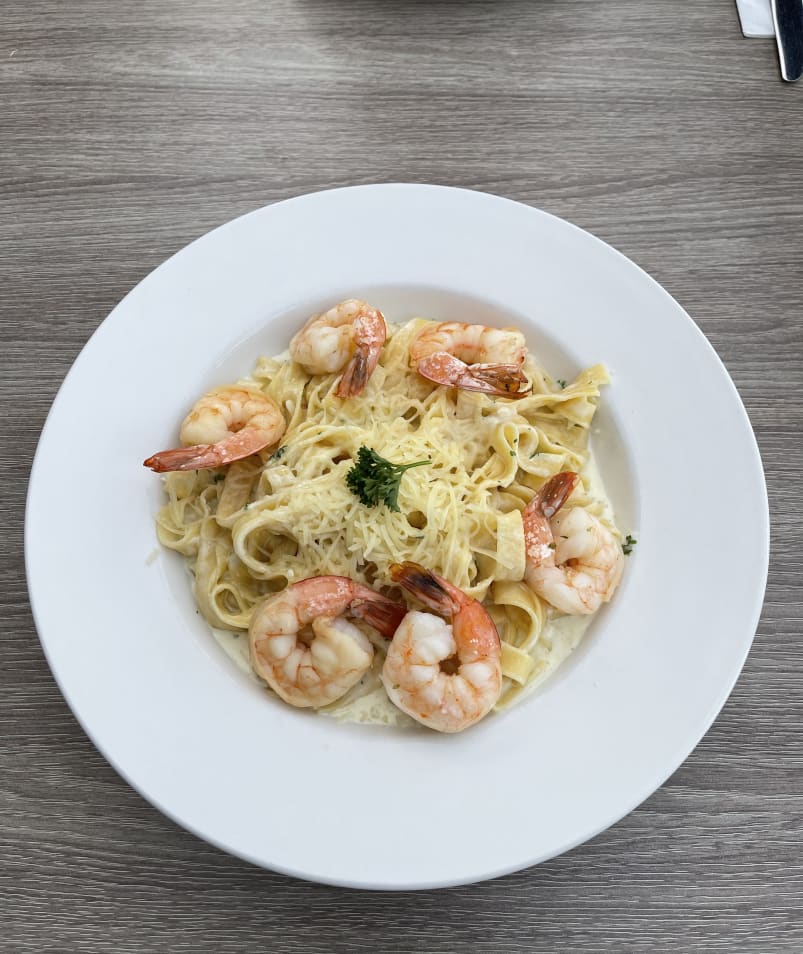 A plate of fettuccine pasta with creamy sauce and garnished with shrimp and parsley, served on a wooden table.