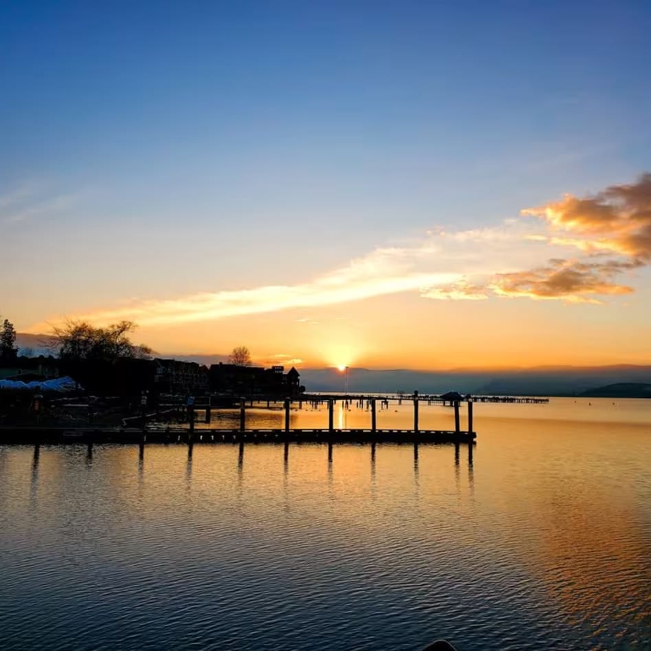 a body of water with a dock in the middle of it and the sun setting in the distance behind it at Hotel Eldorado in Kelowna.