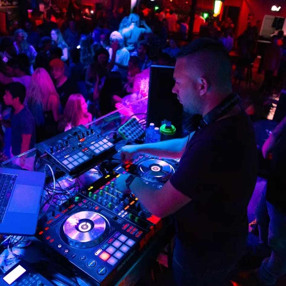 a dj mixing in front of a crowd of people at a party with laptops and sound equipment on the counter