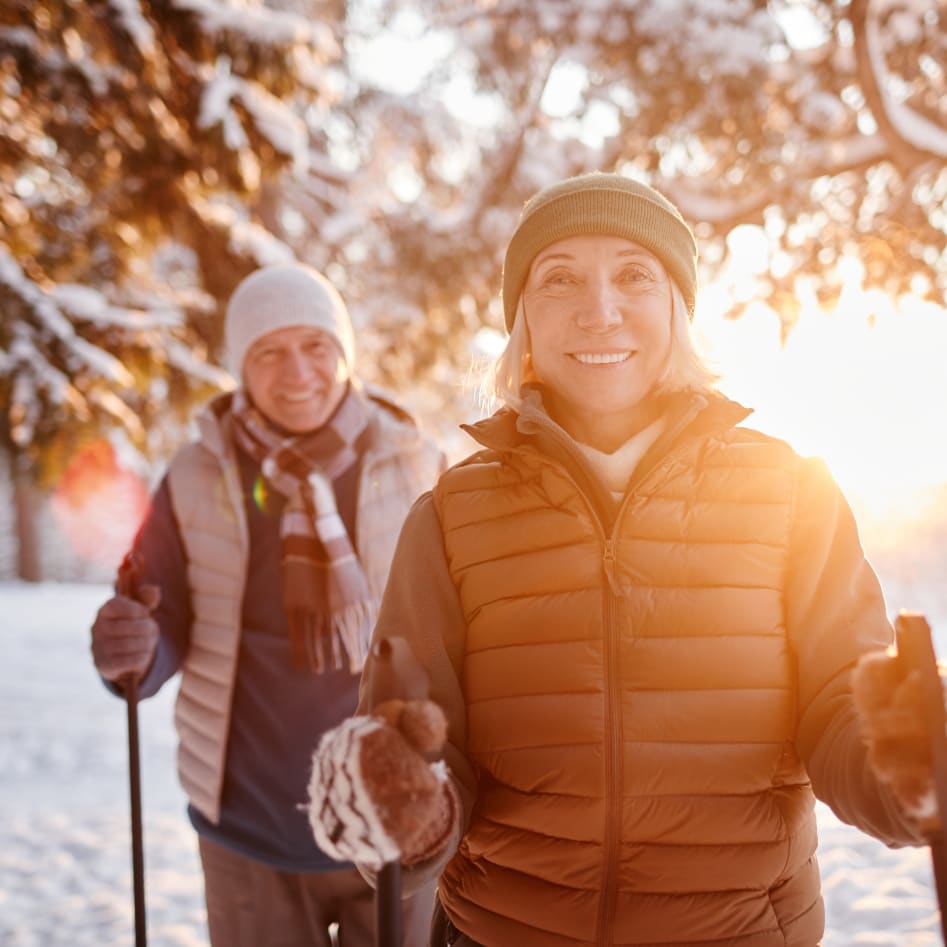 A smiling couple dressed in winter clothing enjoying a snowy landscape with walking poles.