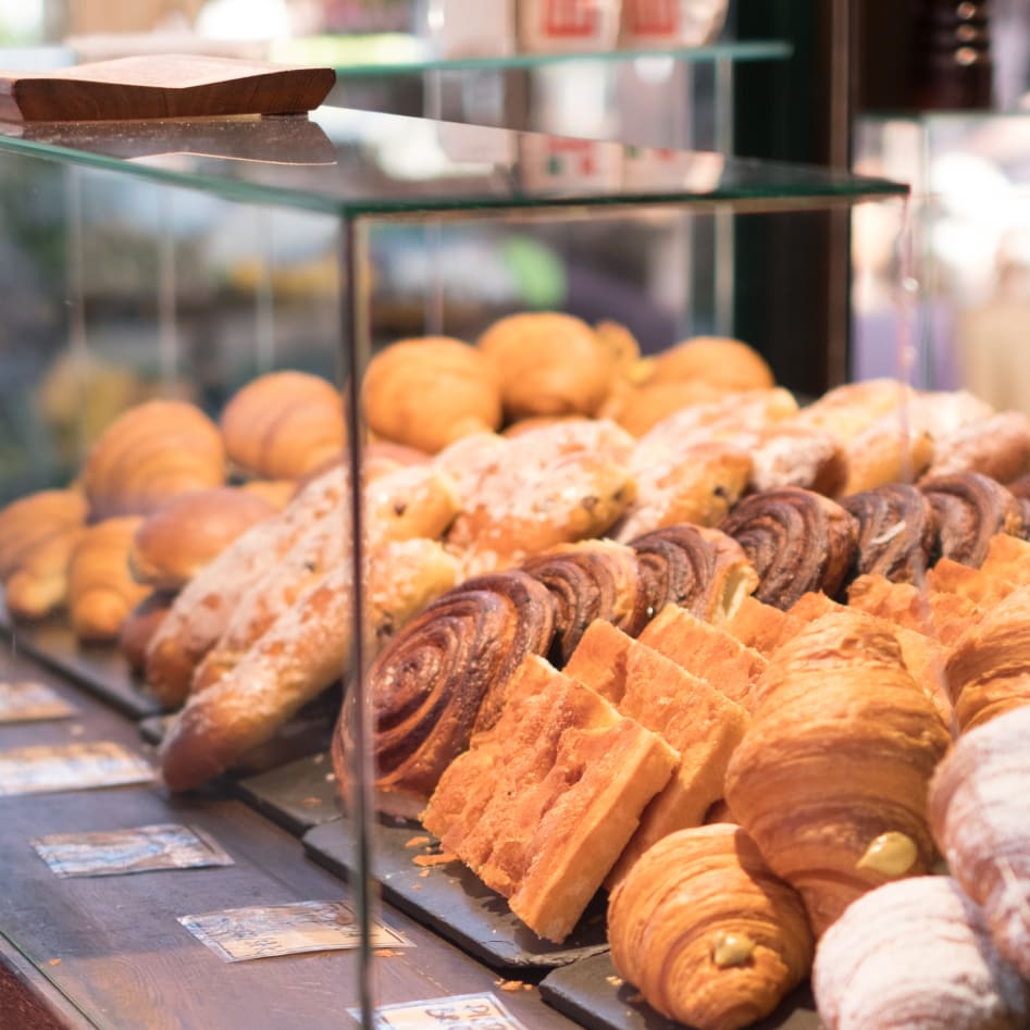 An assortment of pastries, including croissants, scones, and danishes, displayed inside a glass case at a bakery.