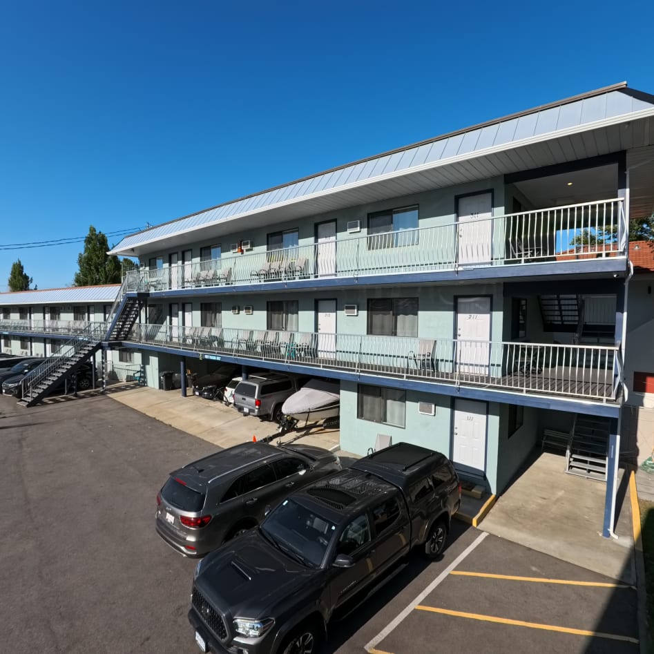 Two-story motel with exterior corridors, parking spaces, and a staircase in Osoyoos on a clear day.