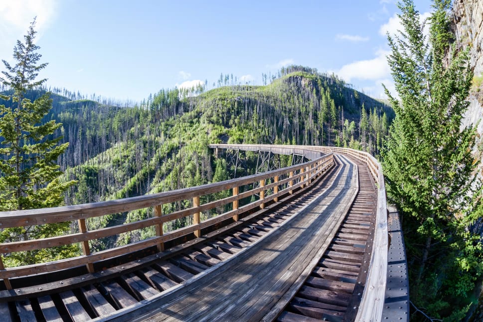 A scenic wooden trestle bridge winding through a forested mountainous area in Kelowna.