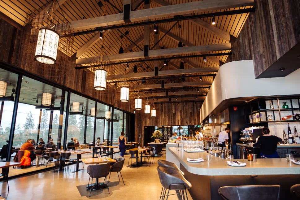 Home Block Restaurant at CedarCreek Estate Winery filled with lots of tables and people sitting at the bar and eating at the tables in front of the windows.