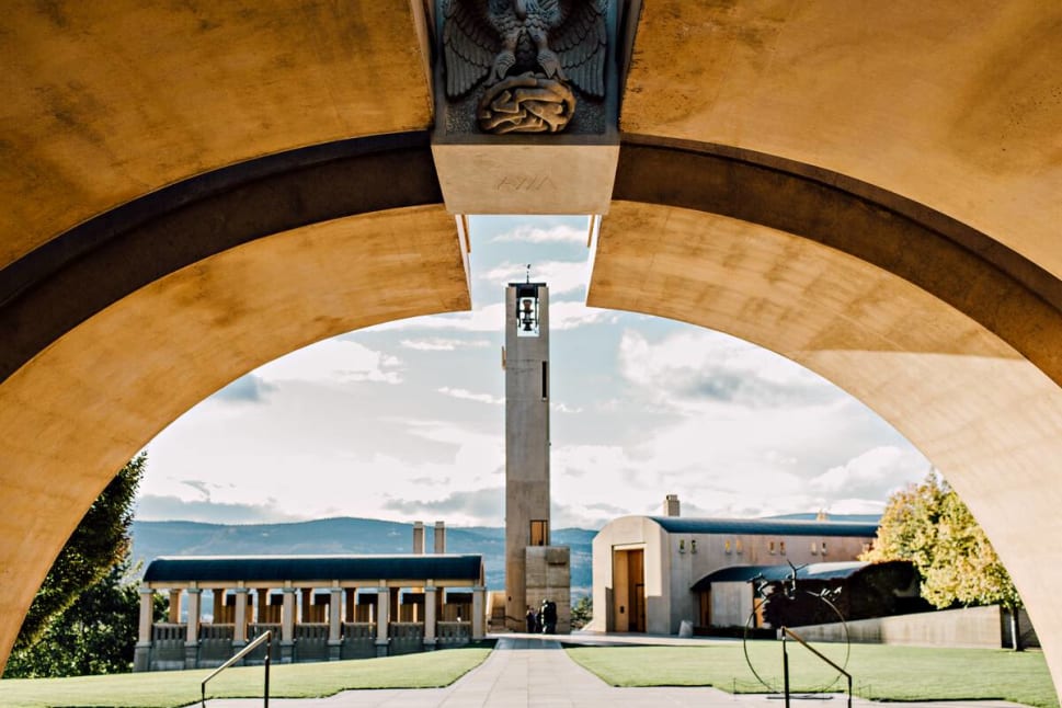 A scenic view of the Mission Hill Family Estate winery framed by an archway, with a tall bell tower in the center and buildings in the background.