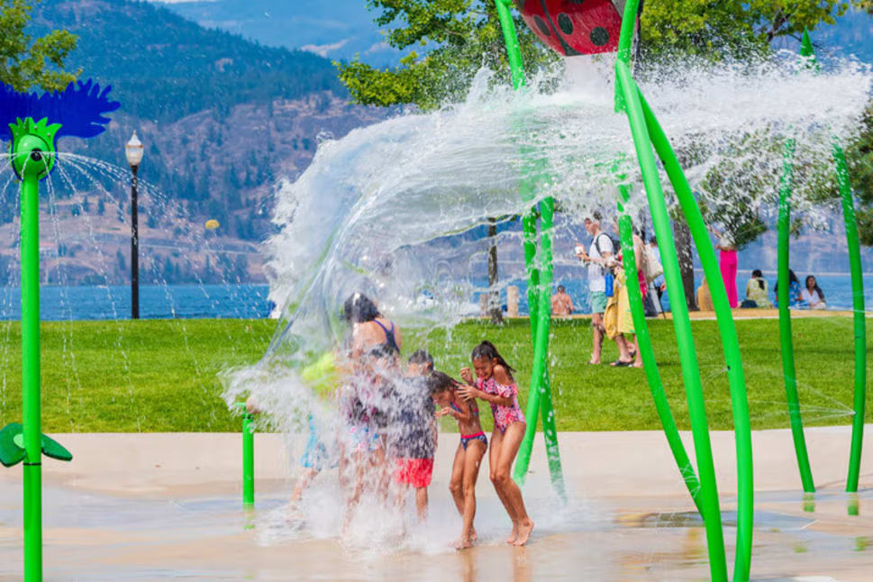 Children playing in a colorful splash park near the waterfront in Kelowna.