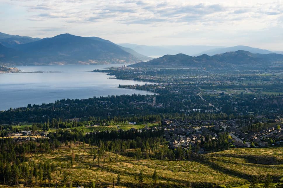 Aerial view of a city by a lake surrounded by mountains under a partly cloudy sky;