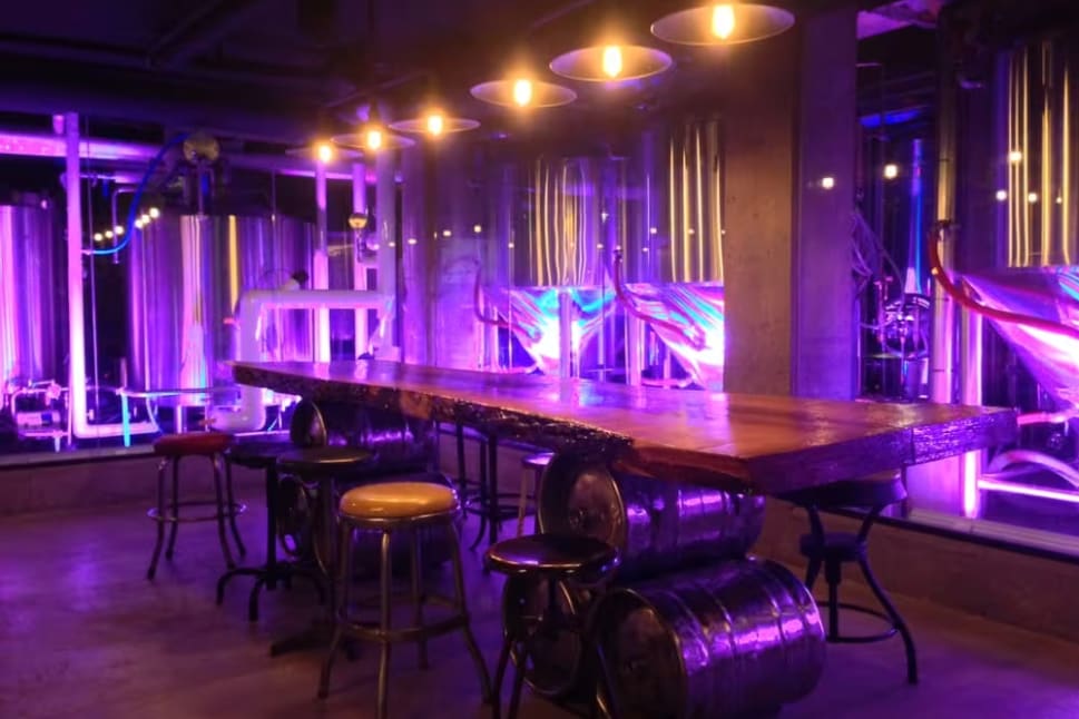 a large wooden table surrounded by stools in a room filled with purple lights and a hammock hanging from the ceiling