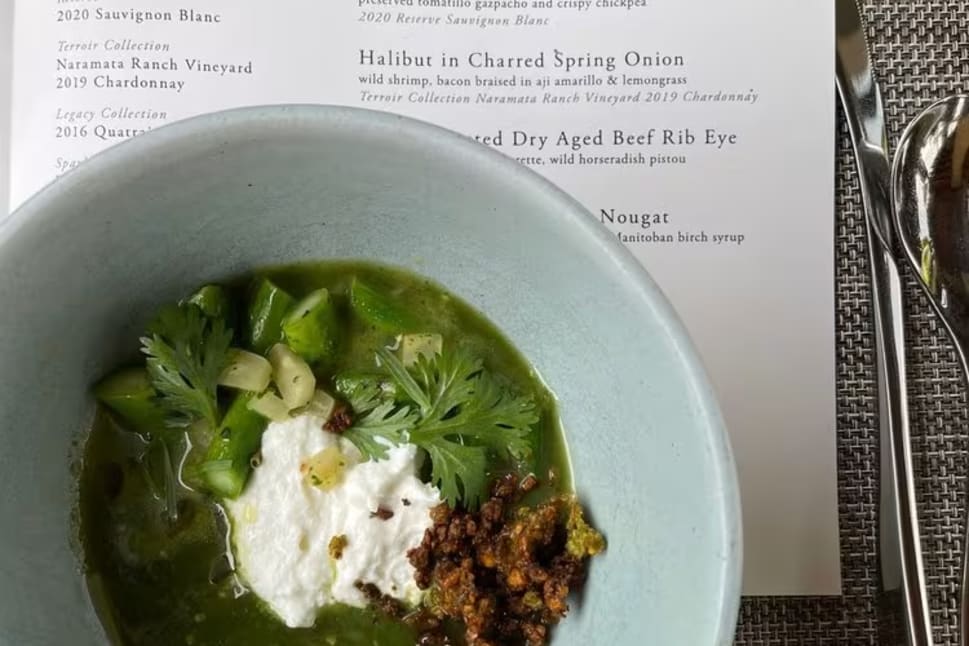 A bowl of green soup with toppings on a table next to a menu from Terrace Restaurant Okanagan Valley.