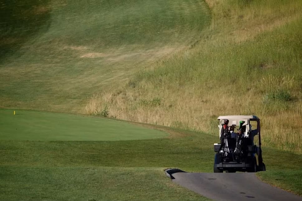 a golf cart driving down a golf course with a golf ball on the ground and a green hill in the background