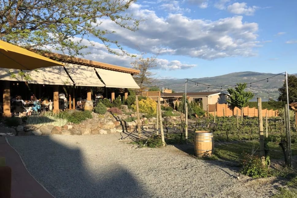 A building with a yellow awning next to a dirt road, surrounded by trees and bushes with a vineyard near Quails' Gate Winery in Kelowna.