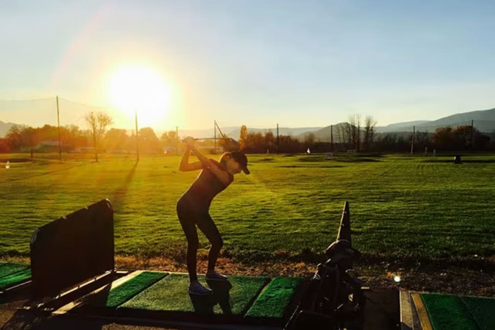 A person swinging a golf club at the Golf Centre Practice Facility in Kelowna during sunset.