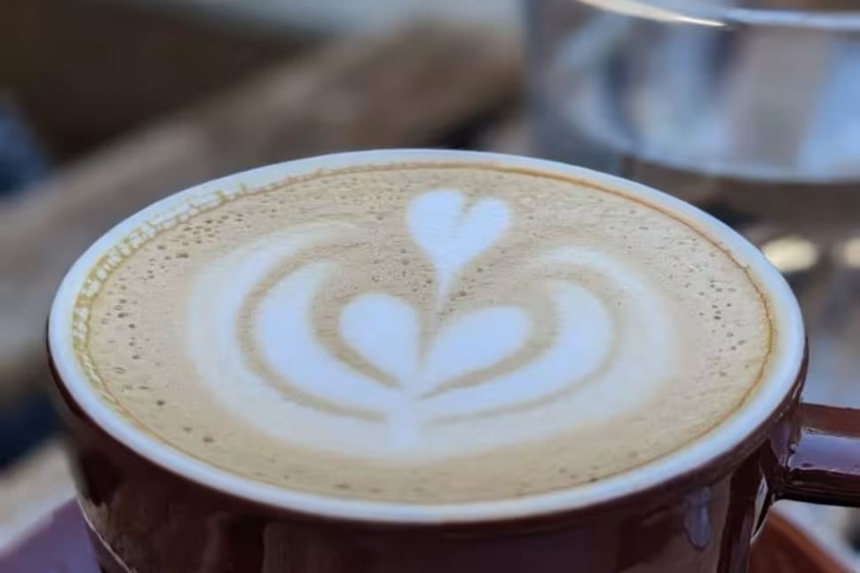 A latte in a dark-colored cup with heart-shaped latte art on top, on a table in Kelowna.