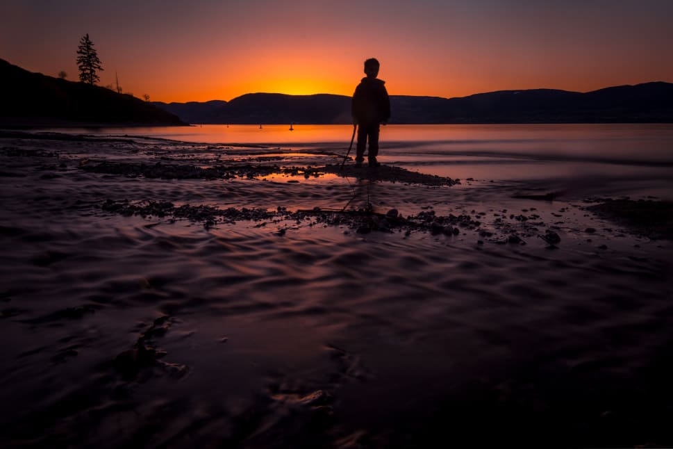 A man is standing on a beach at sunset, looking out at the ocean in the Okanagan region.
