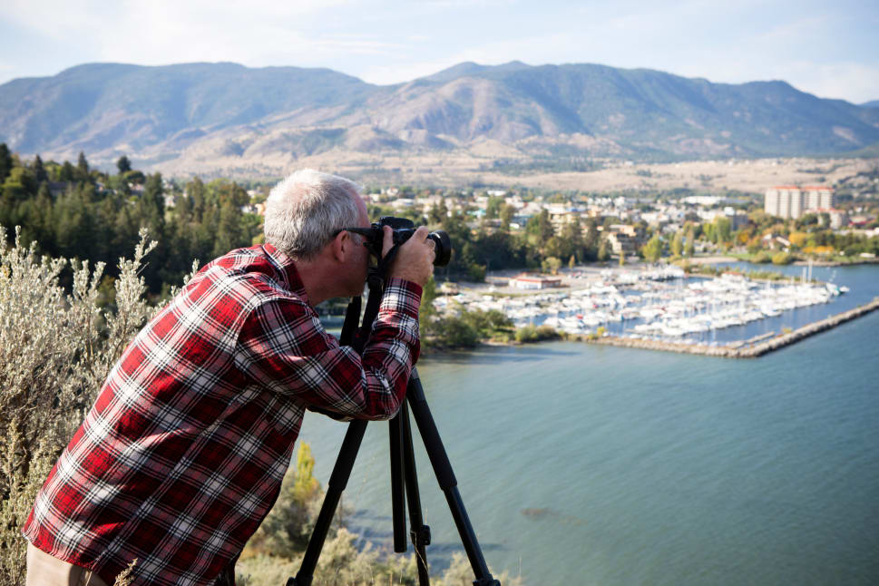A man in a plaid shirt takes a photo with a camera on a tripod overlooking