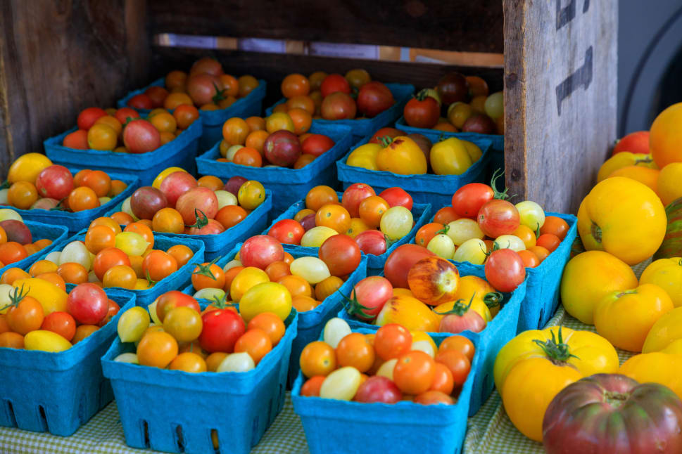 A market stall in Penticton displaying a variety of colorful tomatoes in blue containers.